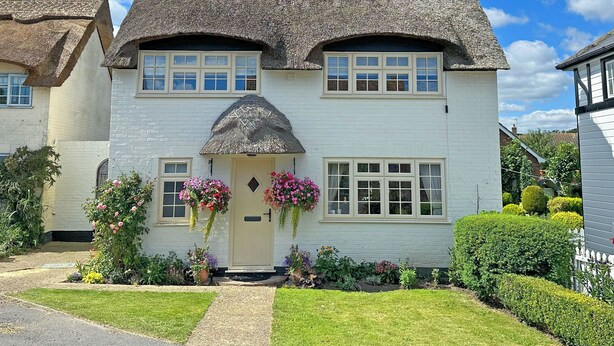 A white house with a thatched roof, a front door, and a small garden with flowers. - Welcoming larger family gatherings. (Winterton-on-Sea)