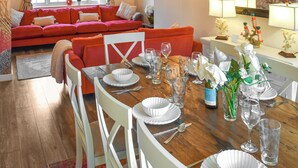 A dining area with a wooden table set for a meal, surrounded by white chairs, and a red sofa in the background. - Welcoming larger family gatherings. (Winterton-on-Sea)