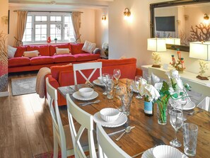 Ein Essbereich mit Holztisch, gedeckt für eine Mahlzeit, umgeben von weißen Stühlen und einer roten Couch im Hintergrund.