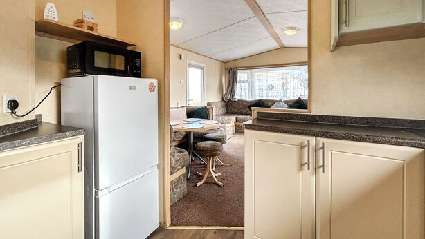 A compact RV kitchen with a refrigerator, microwave, and a dining area with a small table and chairs.