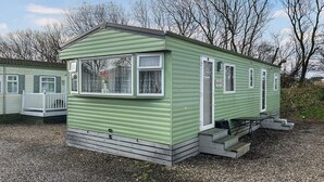 A small, single-story mobile home with a green exterior, white trim, and a small porch.