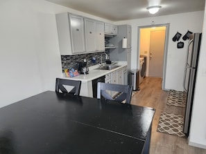 Een kleine keuken met witte kastjes, een zwarte eettafel en een koffiezetapparaat.