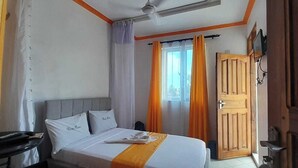 Una habitación de hotel con una cama, una puerta de madera, una ventana con cortinas y un ventilador de techo.