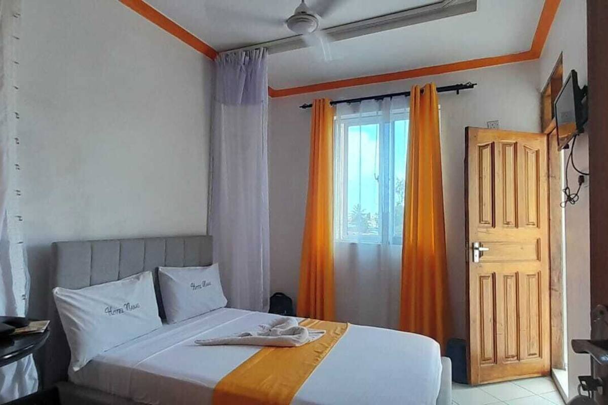 Ein Hotelzimmer mit Bett, einer Holztür, einem Fenster mit Vorhängen und einem Deckenventilator.