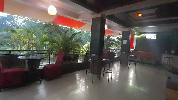 Amplio espacio interior con balcón con vistas a la vegetación, amueblado con sillas y mesas rojas.