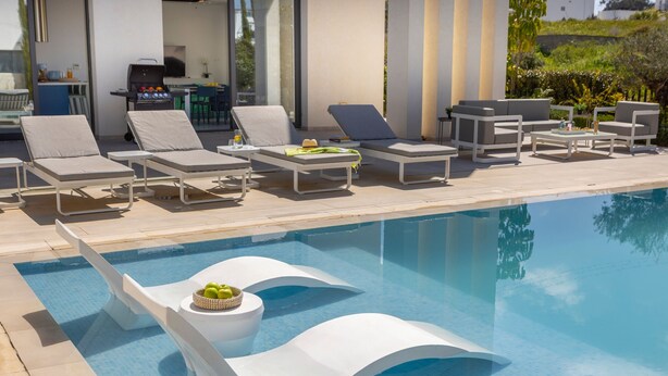 Un área junto a la piscina con sillones de descanso, una barbacoa y una zona de comedor.