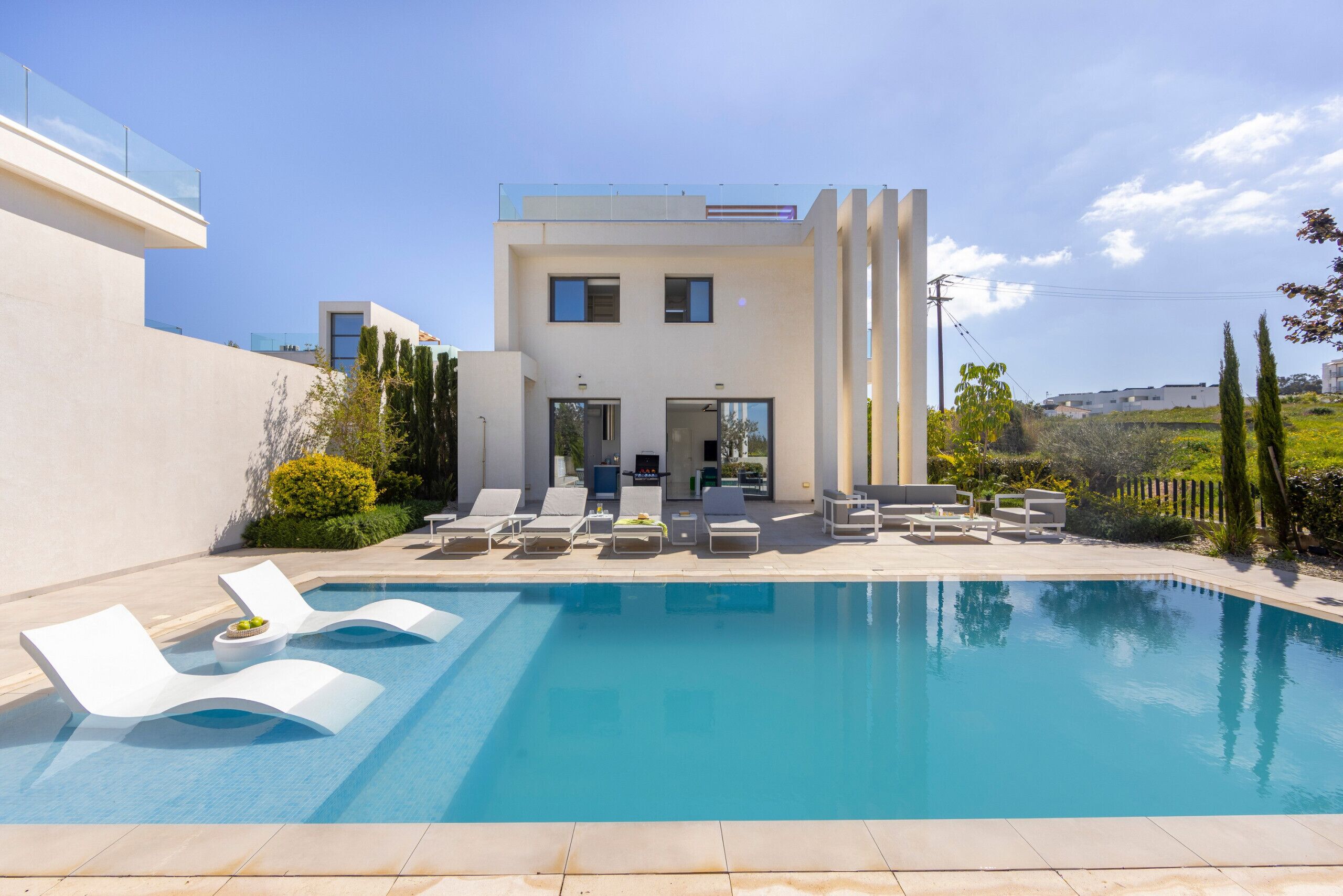 A modern house with a swimming pool, lounge chairs, and a garden.