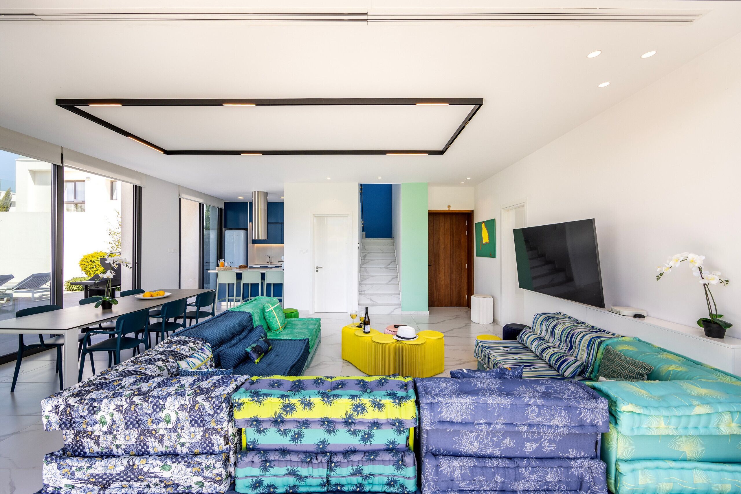 A modern living room with a sofa set, a dining area, and a staircase leading to another level.