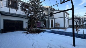 Un quartier résidentiel enneigé avec une piscine, une grande maison dotée d’un garage et un arbre au premier plan.