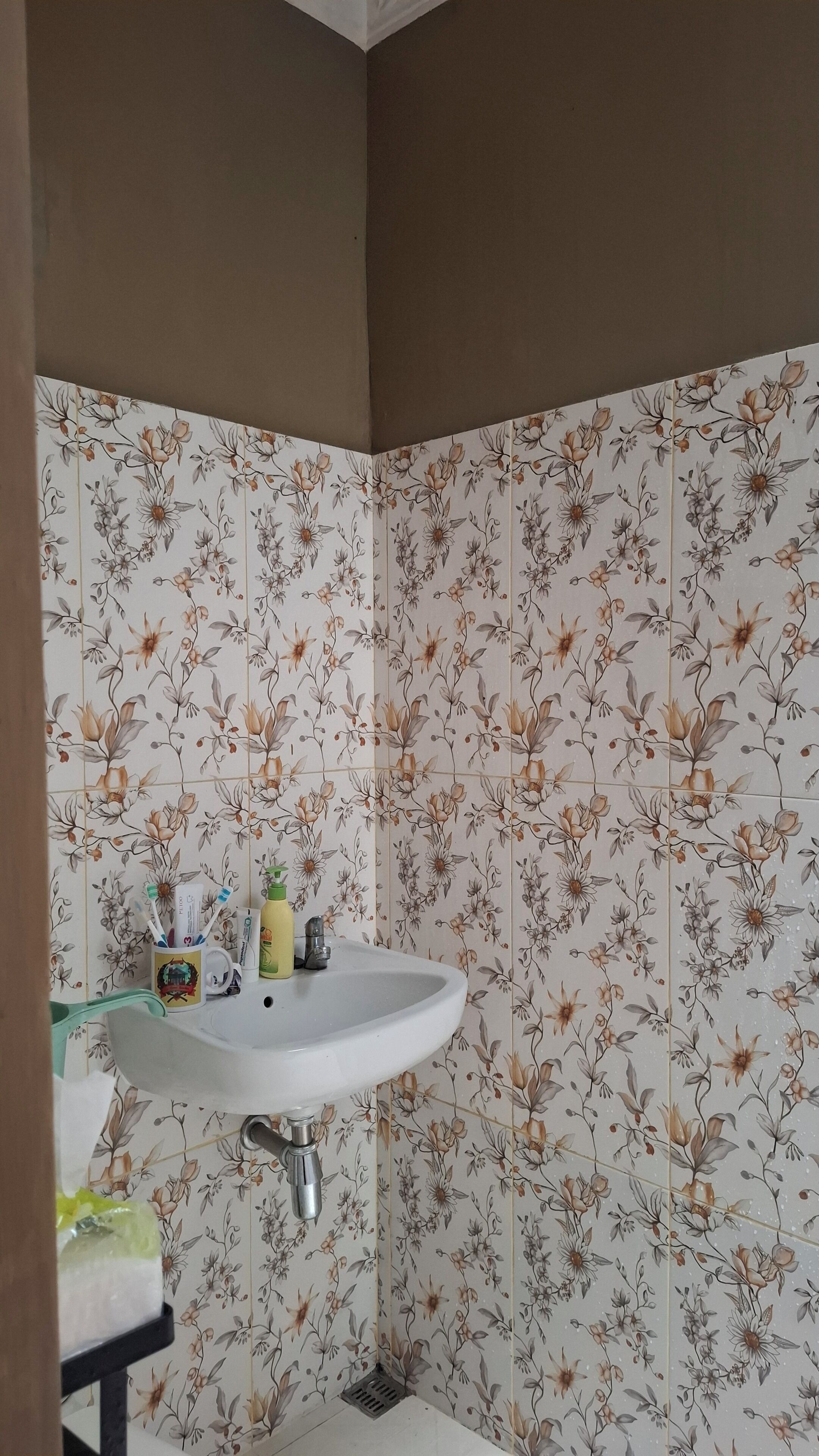 Une salle de bain avec des carreaux à motifs floraux, un lavabo blanc et des articles de toilette posés sur le comptoir.