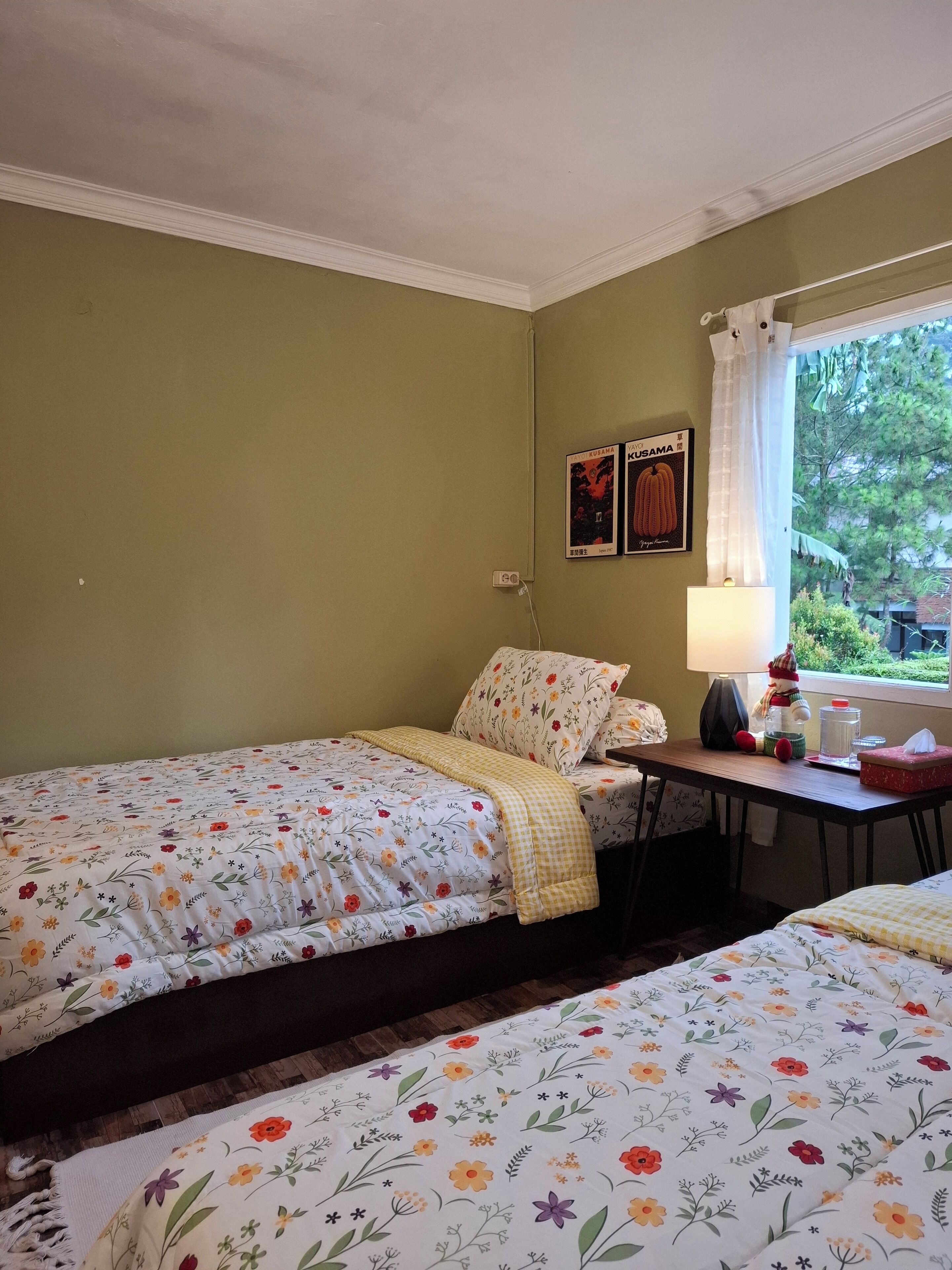 A room with two single beds, a small table with a lamp, and a window with curtains.