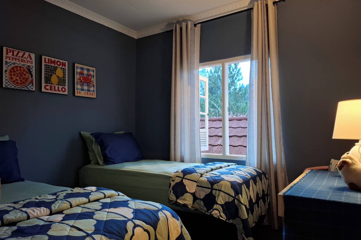 A room with two beds, a window with curtains, a lamp, and wall decorations.