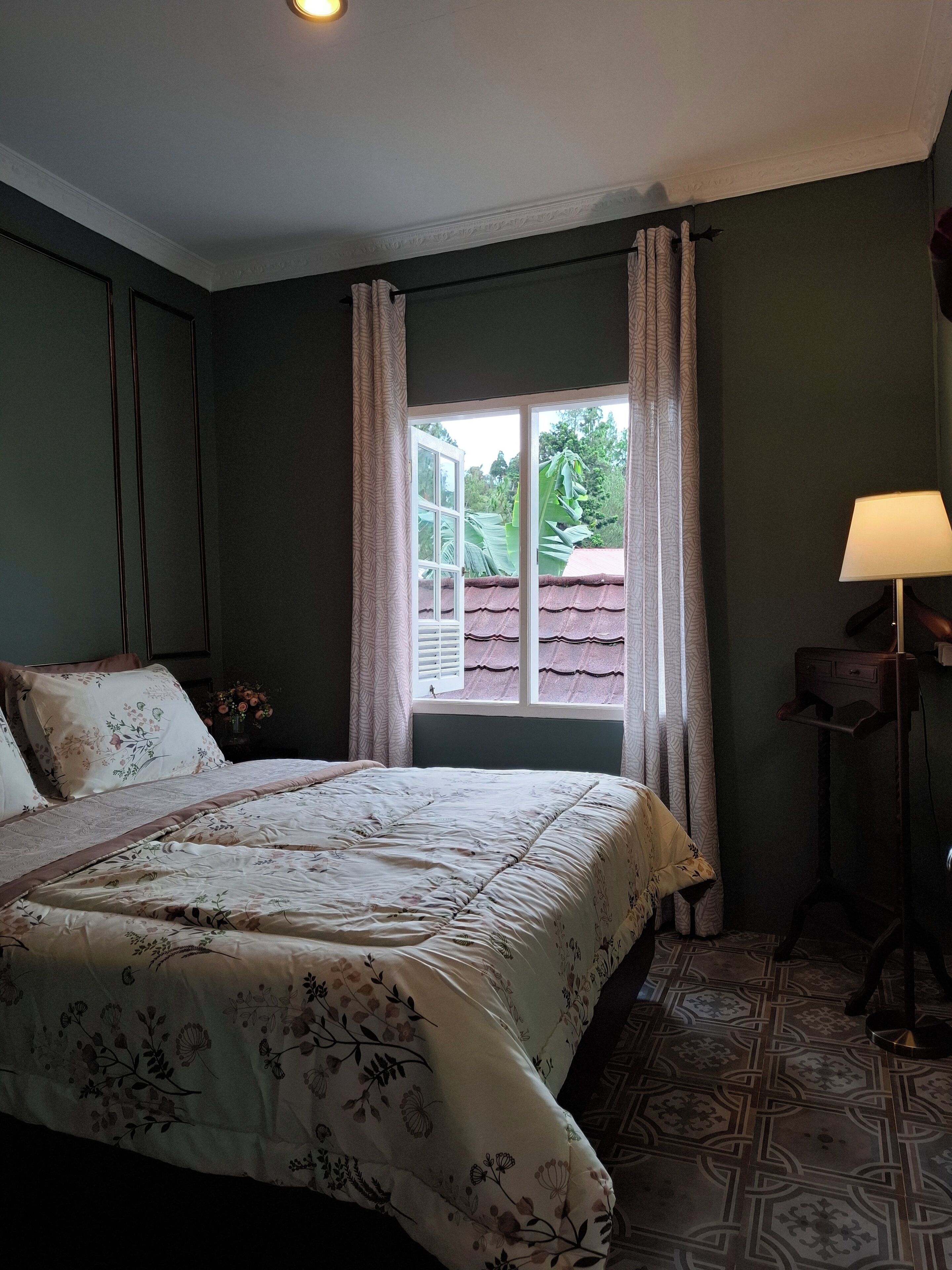 Un dormitorio con una cama grande, una ventana con cortinas, una mesita de noche con lámpara y un suelo con diseño.
