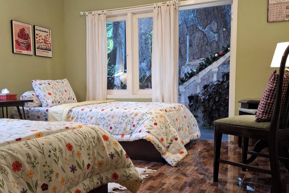 A room with two beds, a chair, a table, and a window with curtains.