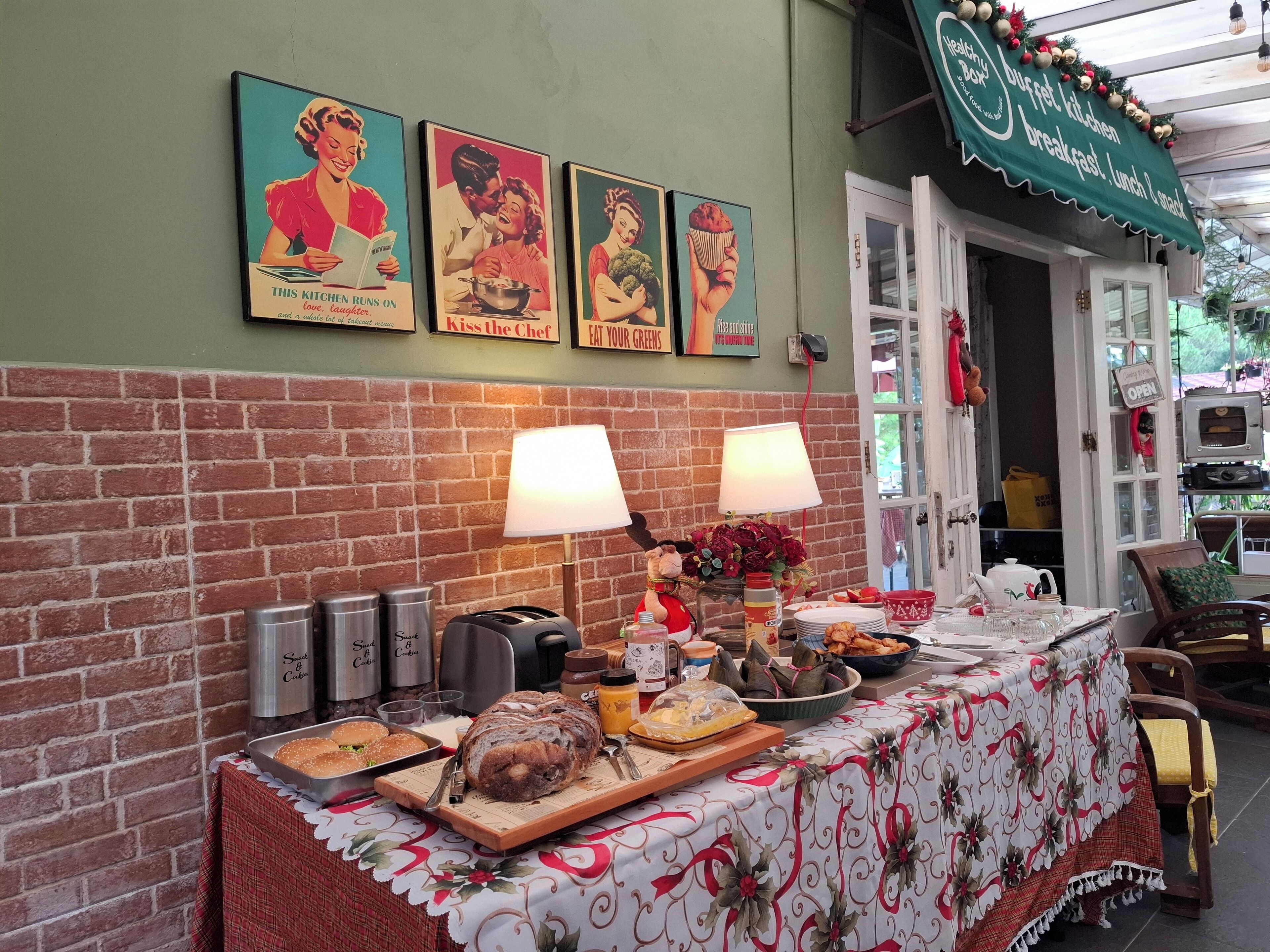A buffet setup with a variety of food items, a brick wall, and a green awning with holiday decorations.