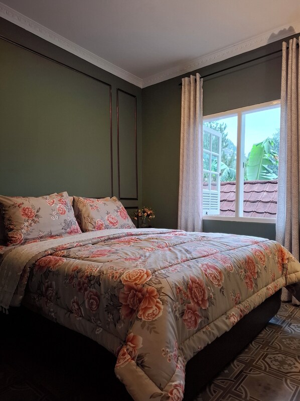 Une chambre à coucher avec une couvre-lit à motifs floraux, une table de chevet ornée d’un vase de fleurs et une fenêtre avec des rideaux.