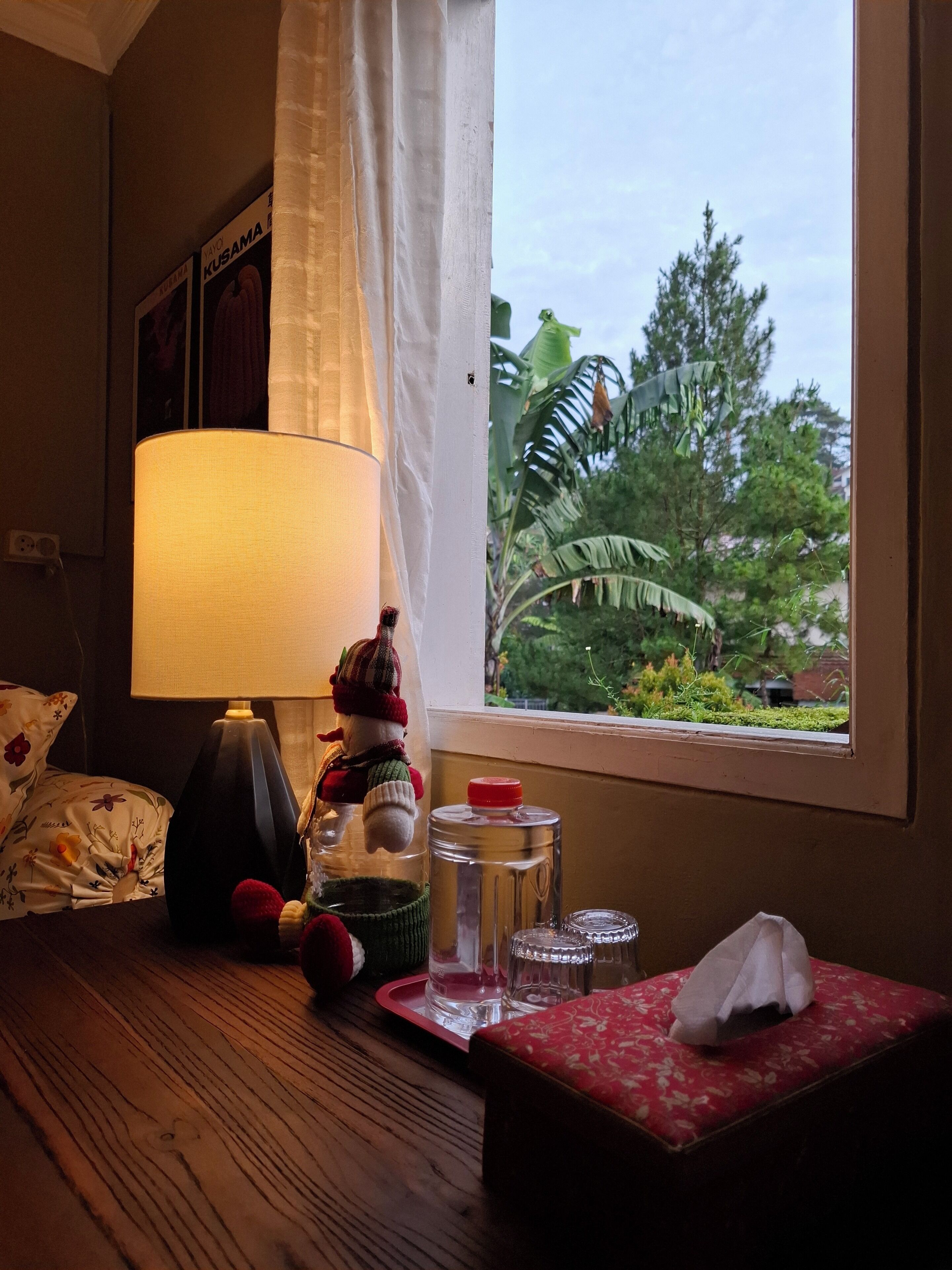 Una stanza con un tavolo di legno, una lampada, una decorazione di pupazzo di neve, un portarrotuli e una finestra vista verde.