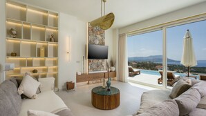 A modern living room with a large TV, a stone accent wall, and a view of the sea. - Villa Verdessa, Divine Sea Views, Private Infinity Pool, Furnished Terrace,. (Crete)