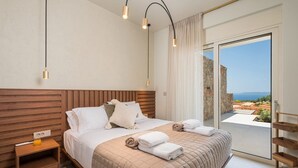 A modern bedroom with a wooden headboard, a large bed with white bedding, a nightstand, and a view of a rocky landscape through a glass door. - Villa Verdessa, Divine Sea Views, Private Infinity Pool, Furnished Terrace,. (Crete)