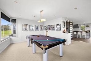 A modern room with a pool table, framed pictures on the wall, and a kitchen area visible through an open door.