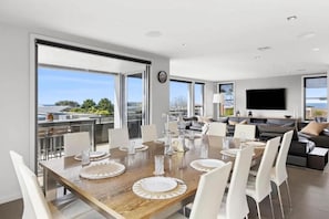 A modern dining area with a large wooden table set for six, surrounded by white chairs.