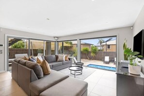 A modern living room with a grey sofa, two black coffee tables, and a large sliding glass door leading to a backyard with a pool.