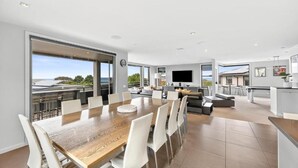 Una cocina moderna con una isla grande, un comedor con mesa de madera y sillas blancas, y una sala de estar con sofá y televisor.