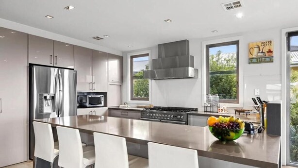 Una cocina moderna con electrodomésticos de acero inoxidable, una isla central con asientos y un amplio ventanal que proporciona luz natural.