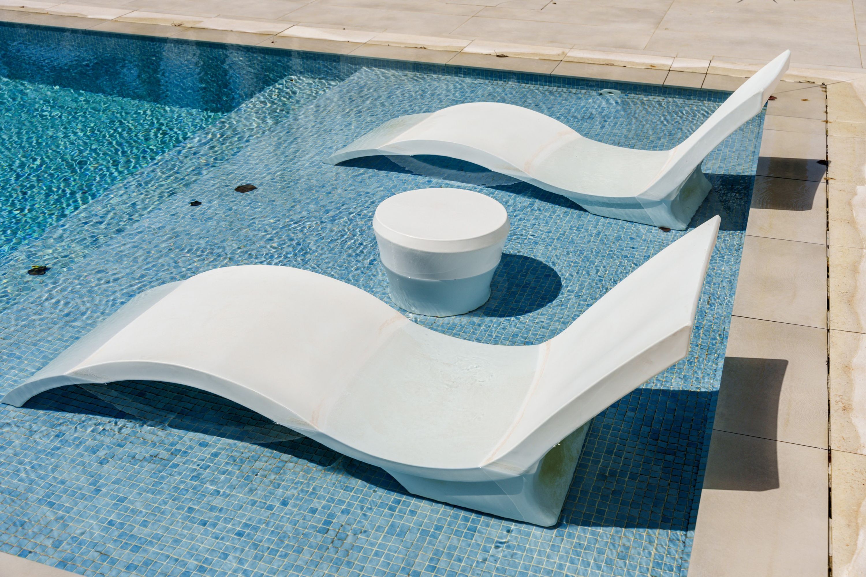 A swimming pool with modern, white, curved lounge chairs and a central white cylindrical object.