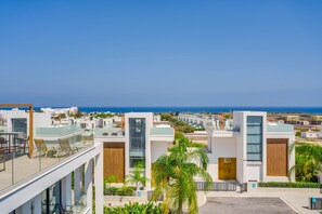 A modern residential area with contemporary architecture, including glass balconies and wooden accents, overlooking a coastal landscape. - Protaras By the Bay Villa 19 (Paralimni)