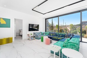 A modern living room with a large window, a flat-screen TV, a sofa set, and a small table. - Protaras By the Bay Villa 19 (Paralimni)