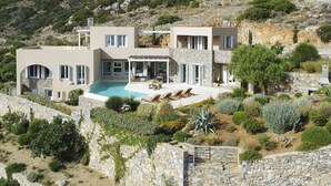 Een moderne villa met zwembad, stenen muren en een tuin met diverse planten.