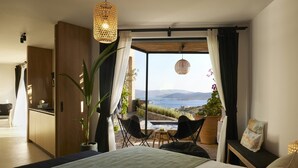 Een slaapkamer met een bed, een kamerplant, een zithoek met stoelen en uitzicht op zee.