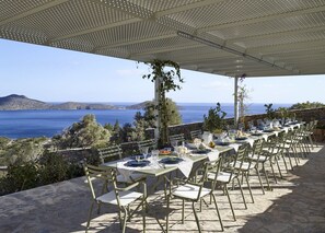 An outdoor dining area with tables set for a meal, overlooking a scenic view of the sea and hills. - Villa Olivene, Divine Sea Views, Private Infinity Pool, Furnished Terrace,. (Crete)