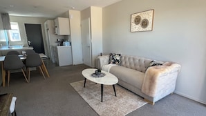A modern living room with a sofa, coffee table, and dining area. - Modern 2BR St Albans Near CBD, Stadium & The Palms mall (Christchurch)