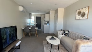 A modern living room with a flat-screen TV, a sofa, a coffee table, and a dining area in the background. - Modern 2BR St Albans Near CBD, Stadium & The Palms mall (Christchurch)