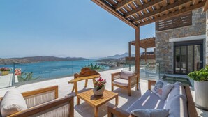 Eine Terrasse mit Holzmöbeln, einer Steinmauer und Meerblick.