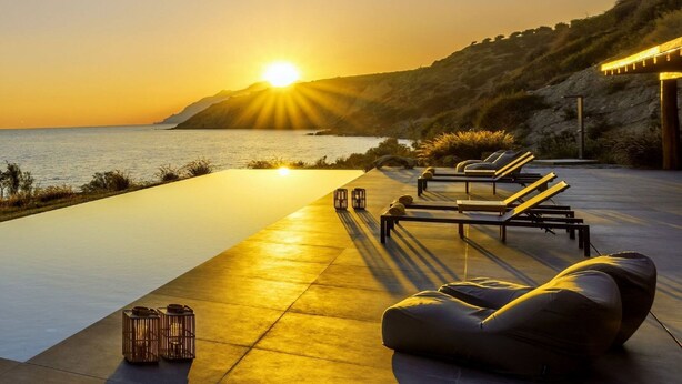 En vacker solnedgångsbild över en pool med solstolar och en pergola.