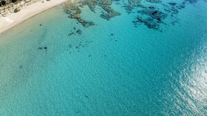 Ett flygbildsbild av ett kustområde med klart turkosfärgat vatten, en sandstrand och ett semesterområde med flera byggnader.