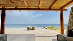 Utsikt över stranden från ett takförsett utomhusområde med en stenmur och en träpergola.