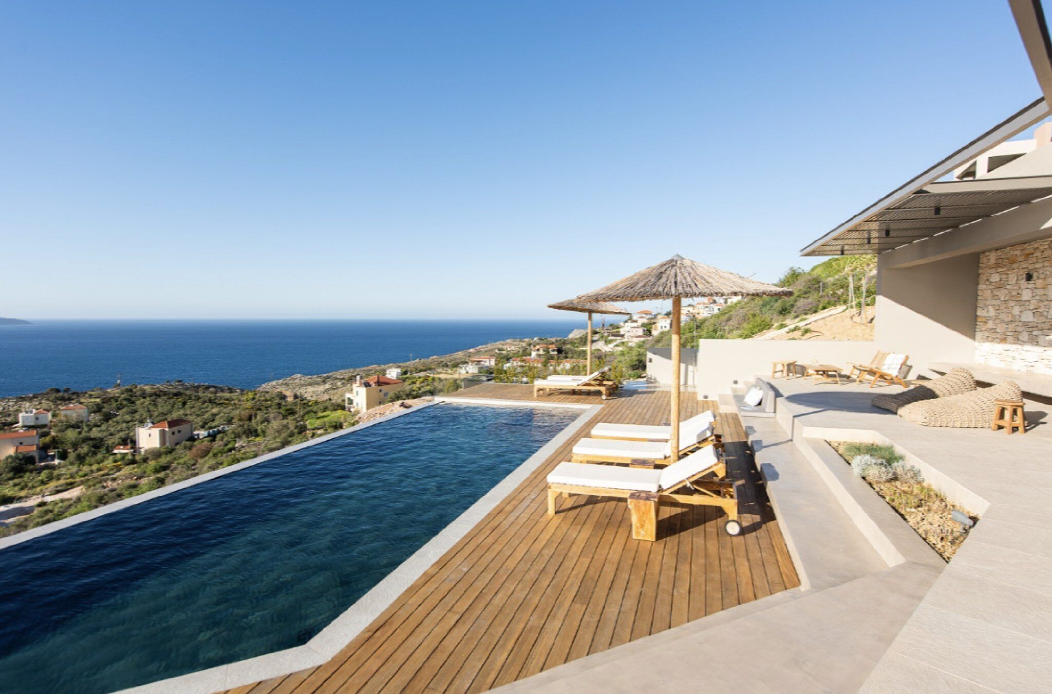 Eine Holzterrasse mit Pool, Liegestühlen und Blick auf das Meer.