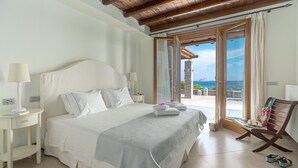A bedroom with a large bed, a wooden ceiling, a view of the sea, and a chair with a colorful bag. - Seafront Villa Solaryth, Divine Sea Views, Private Pool, Furnished Terrace,. (Crete)