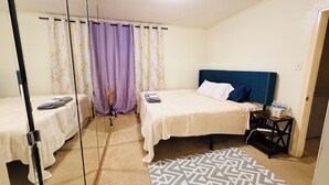 Een hotelkamer met twee bedden, een spiegel, een kamerkleed met patroon en een nachtkastje met toiletartikelen.
