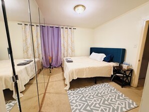 Ein Hotelzimmer mit zwei Betten, einem Spiegel, einem gemusterten Teppich und einem Nachttisch mit Toilettenartikeln.