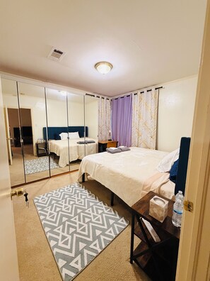 Habitación de hotel con cama, mesita de noche, espejo y alfombra estampada.