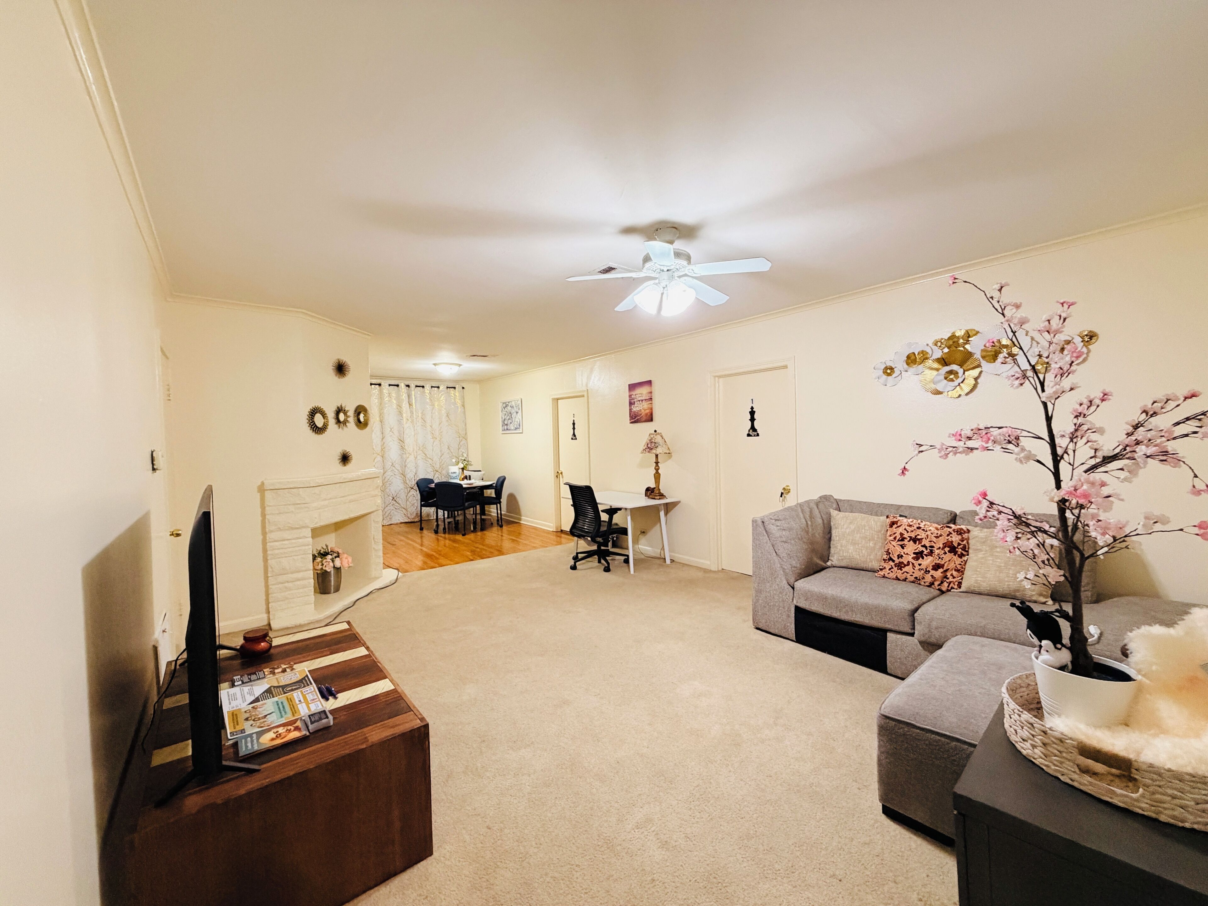 A living room with a flat-screen TV, a fireplace, a dining area with a table and chairs, a sofa, and a ceiling fan.