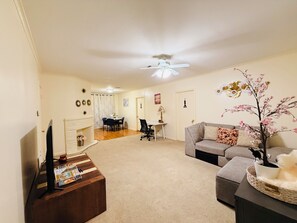 Ein Wohnzimmer mit Flachbildfernseher, Kamin, Essbereich mit Tisch und Stühlen, Sofa und Deckenventilator.