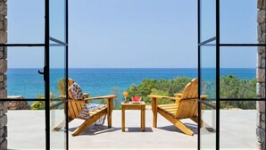 Un balcon avec deux chaises en bois et une petite table, d’où l’on peut admirer une mer bleue et limpide et une végétation luxuriante.