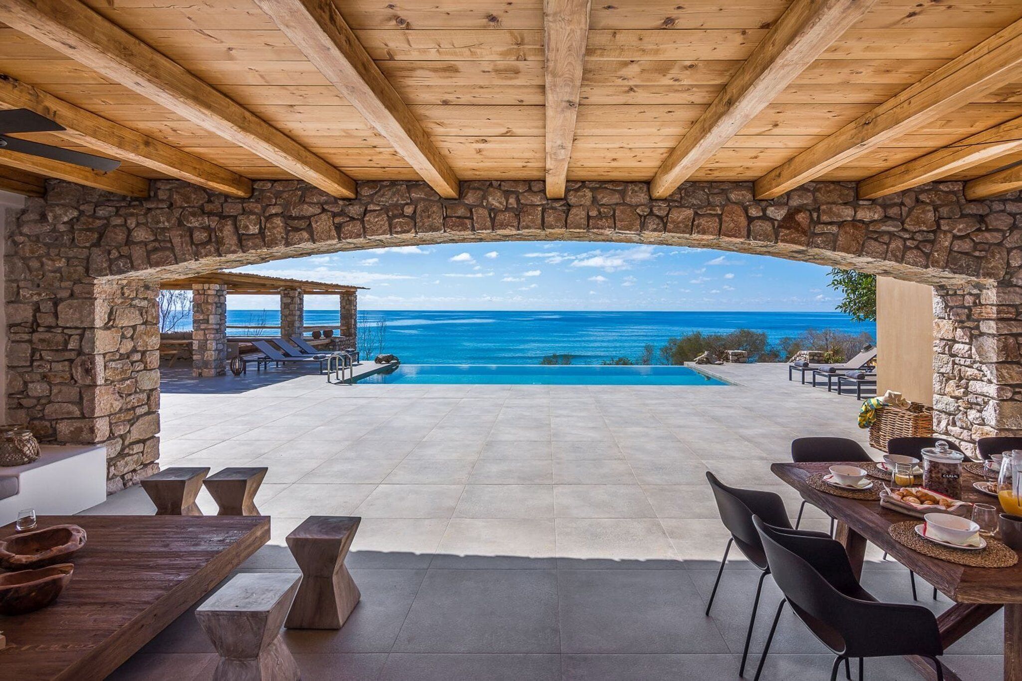 Un patio ad arco in pietra con piscina e sedie a sdraio, con vista sul mare cristallino.