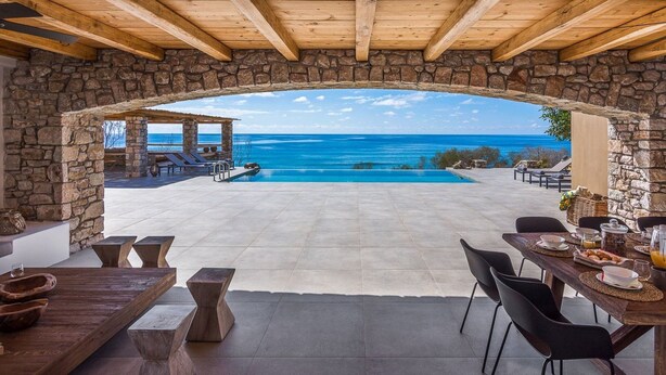 Une terrasse en pierre, agrémentée d’une piscine et de chaises longues, qui offre une vue imprenable sur une mer d’un bleu profond.